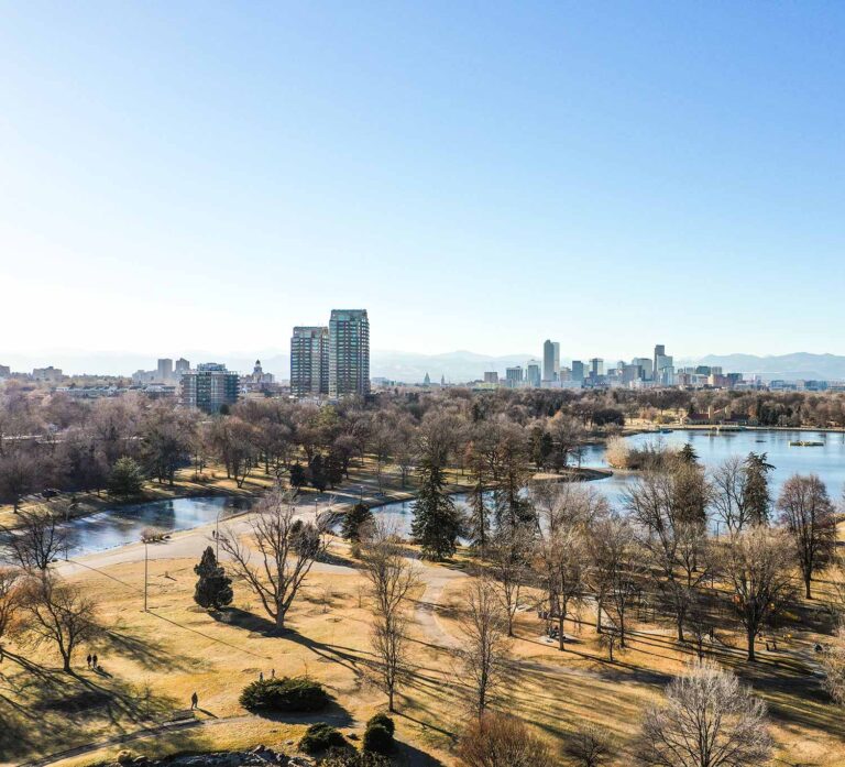 An image of Denver, CO with a park, lakes and the city and mountains in the background